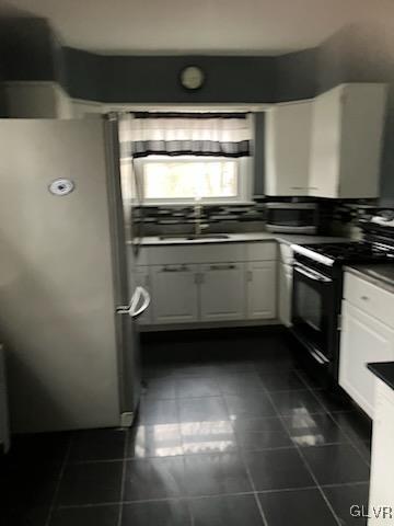 kitchen featuring electric range, dark tile patterned floors, dark countertops, white cabinetry, and freestanding refrigerator