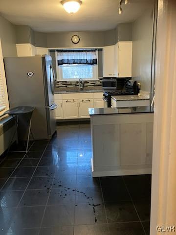 kitchen featuring dark tile patterned flooring, a sink, dark countertops, appliances with stainless steel finishes, and white cabinets