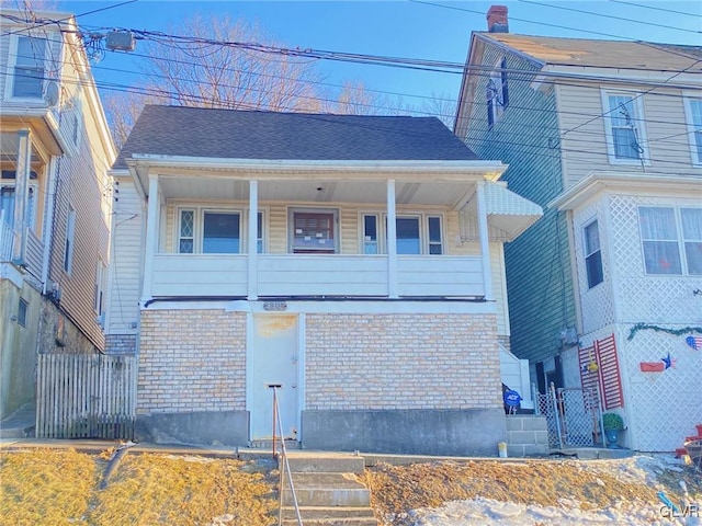 view of front of house featuring roof with shingles, fence, and brick siding