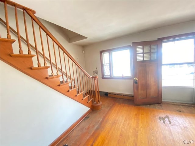 entrance foyer with a baseboard heating unit, stairs, baseboards, and wood finished floors