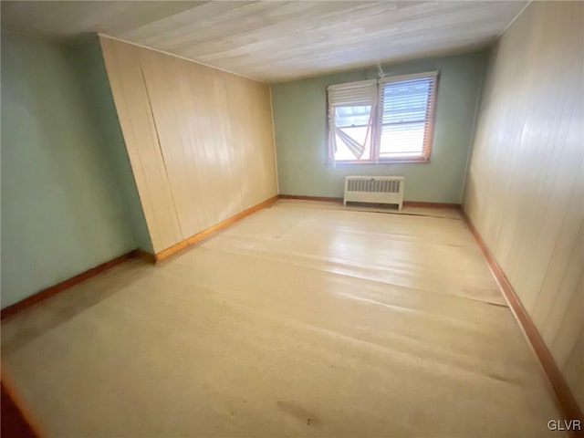 spare room with baseboards, wood walls, and radiator heating unit