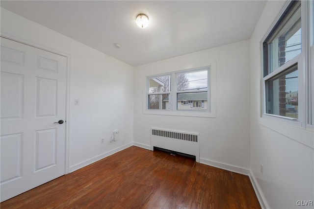 spare room featuring radiator heating unit, baseboards, and dark wood-type flooring