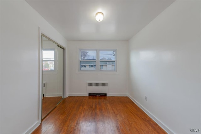 empty room with baseboards, radiator heating unit, and wood finished floors