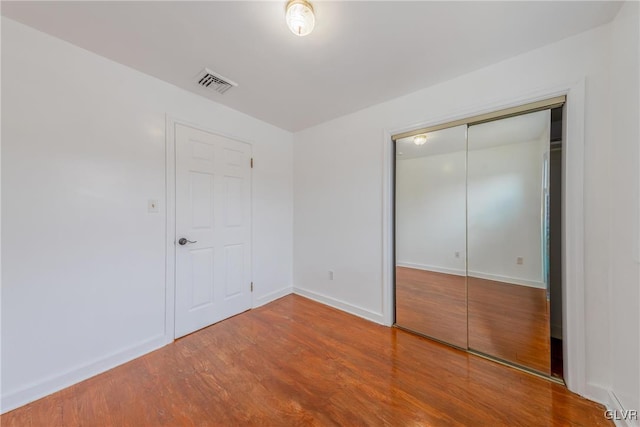 unfurnished bedroom featuring a closet, wood finished floors, visible vents, and baseboards