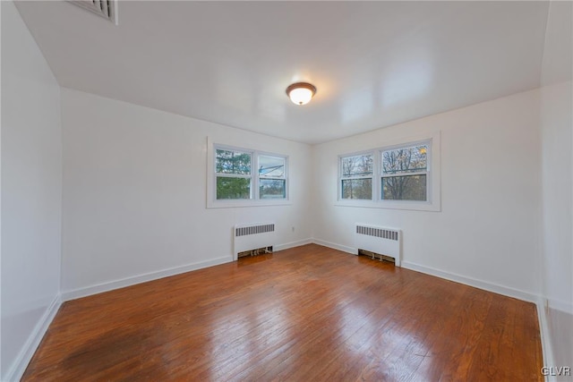 unfurnished room with baseboards, wood-type flooring, and radiator