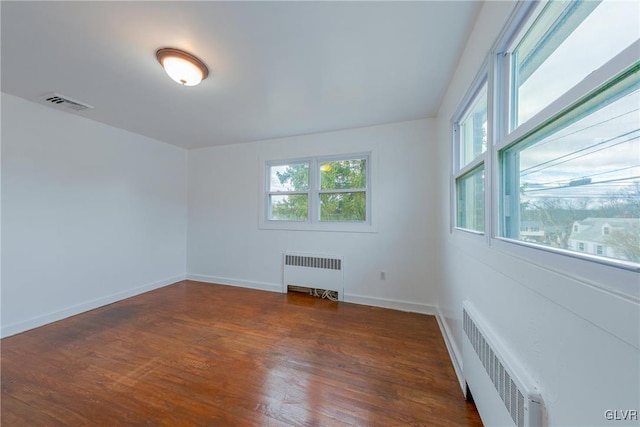 empty room with plenty of natural light, radiator heating unit, and wood finished floors