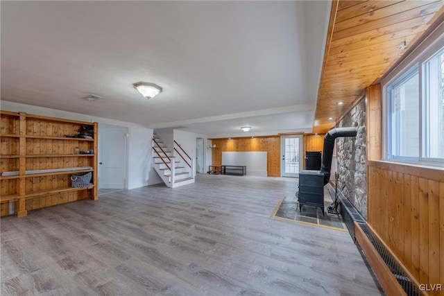 unfurnished living room with stairway, wood finished floors, a wood stove, and wooden walls