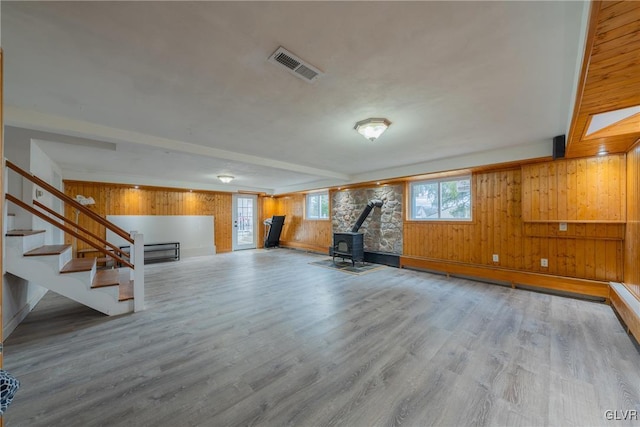 unfurnished living room with a wood stove, stairs, visible vents, and wood finished floors