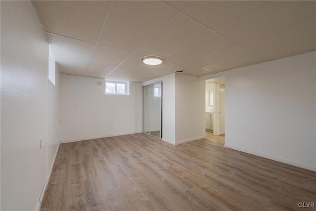 below grade area with a paneled ceiling, baseboards, and wood finished floors