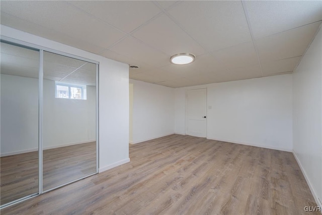 basement featuring baseboards, a drop ceiling, and wood finished floors