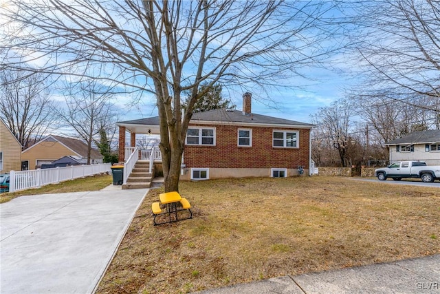 view of front of home featuring brick siding, a chimney, covered porch, fence, and a front lawn