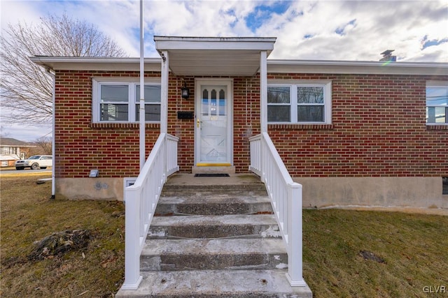 doorway to property featuring brick siding and a lawn