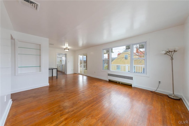 unfurnished living room with baseboards, visible vents, built in features, radiator, and light wood-style floors