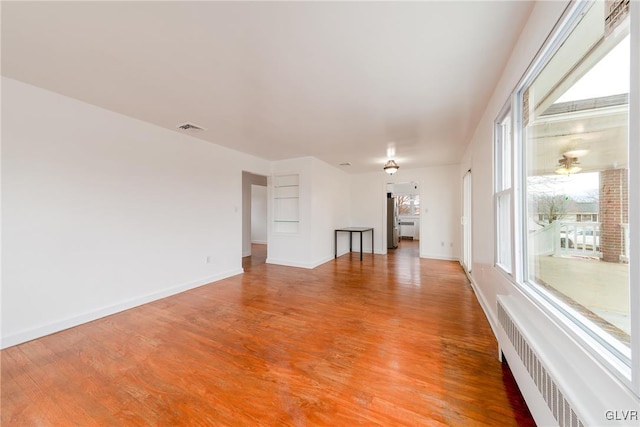 spare room featuring radiator heating unit, light wood-type flooring, visible vents, and baseboards