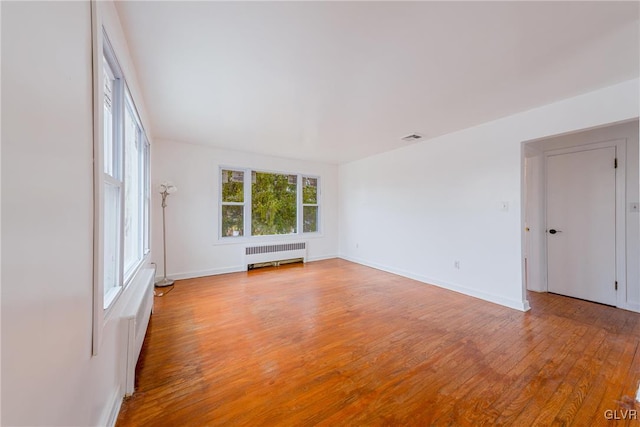 spare room featuring light wood finished floors, radiator heating unit, visible vents, and baseboards