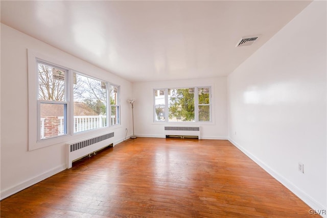 unfurnished room featuring radiator heating unit, visible vents, wood-type flooring, and baseboards