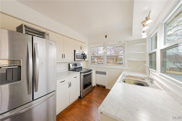 kitchen with dark wood finished floors, radiator, light countertops, appliances with stainless steel finishes, and a sink