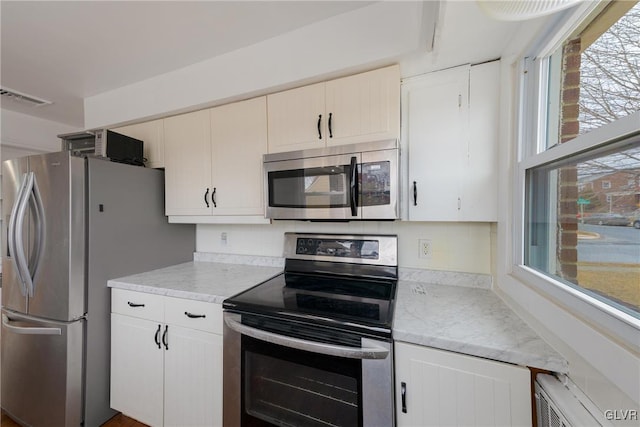 kitchen with light stone countertops, visible vents, appliances with stainless steel finishes, and white cabinets