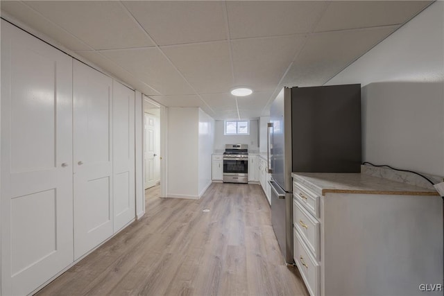 kitchen with a paneled ceiling, white cabinetry, light countertops, appliances with stainless steel finishes, and light wood-type flooring