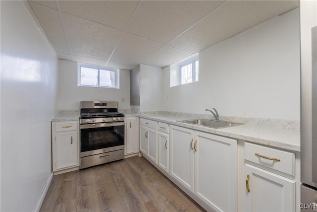 kitchen featuring stainless steel gas range oven, white cabinets, a drop ceiling, wood finished floors, and a sink