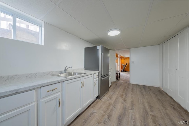 kitchen with a sink, white cabinetry, light wood-style floors, freestanding refrigerator, and light stone countertops