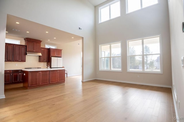 7013 Oak Ln, East Allen Twp, PA 18014 - kitchen featuring freestanding refrigerator, light countertops, a towering ceiling, decorative backsplash, and light wood-type flooring