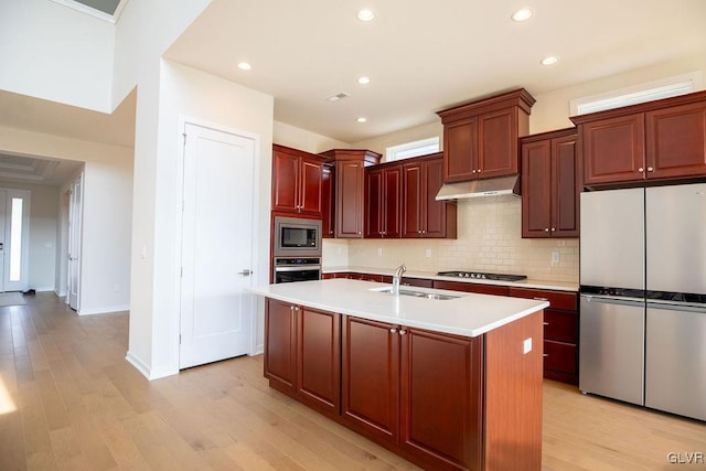 kitchen with under cabinet range hood, a sink, light countertops, appliances with stainless steel finishes, and light wood finished floors