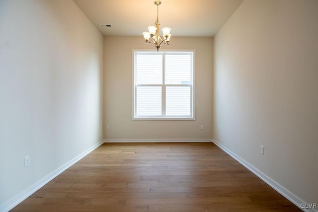 spare room with baseboards, visible vents, an inviting chandelier, and wood finished floors