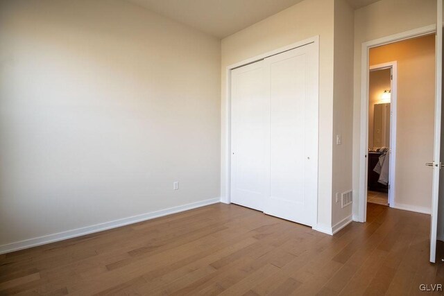 unfurnished bedroom with a closet, visible vents, baseboards, and wood finished floors