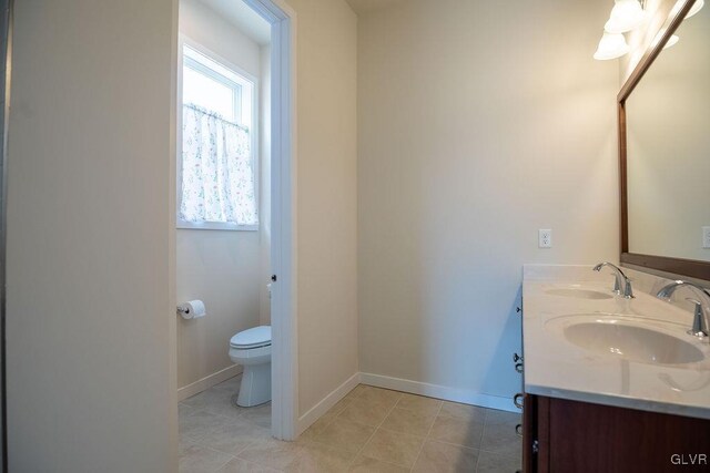 full bathroom featuring toilet, double vanity, baseboards, and a sink