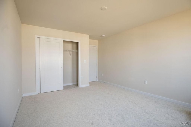 unfurnished bedroom with a closet, light colored carpet, and baseboards