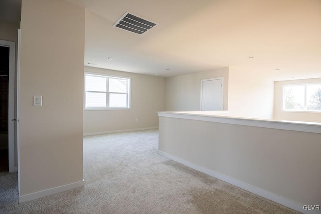 hall with light carpet, visible vents, a wealth of natural light, and baseboards