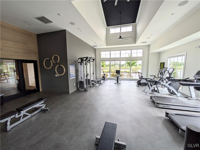 gym featuring visible vents, a high ceiling, a ceiling fan, wood walls, and baseboards