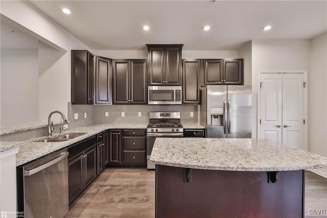 kitchen with stainless steel appliances, a breakfast bar, a sink, light wood-style floors, and light stone countertops