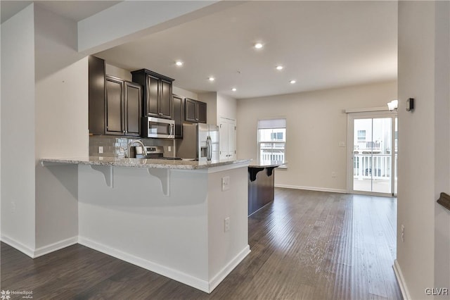 kitchen with dark wood-type flooring, appliances with stainless steel finishes, decorative backsplash, and a breakfast bar area