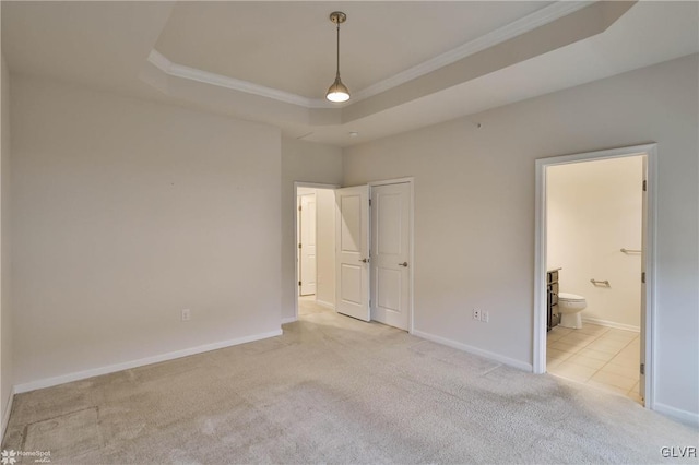 unfurnished bedroom featuring ensuite bath, carpet flooring, a raised ceiling, and baseboards