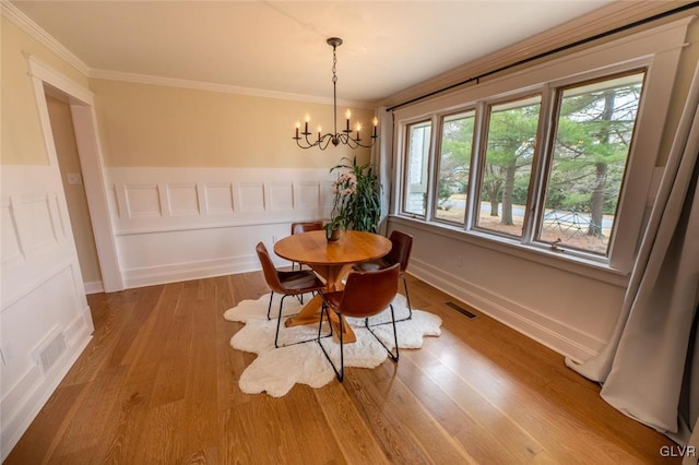 dining space featuring a chandelier, visible vents, crown molding, and wood finished floors