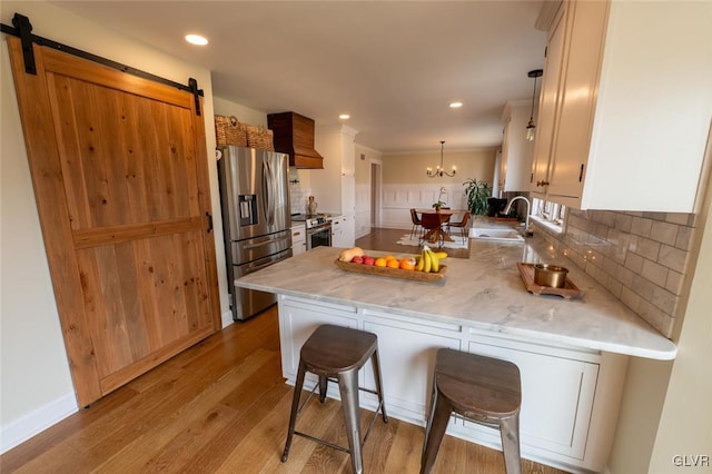 kitchen featuring a barn door, stainless steel appliances, a peninsula, a sink, and backsplash