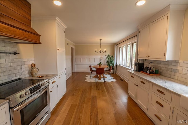 kitchen with crown molding, light wood-style flooring, white cabinetry, premium range hood, and stainless steel electric range