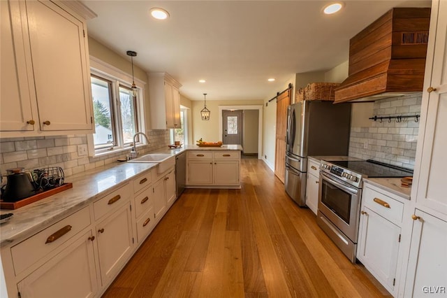 kitchen with a barn door, stainless steel appliances, a peninsula, a sink, and custom exhaust hood