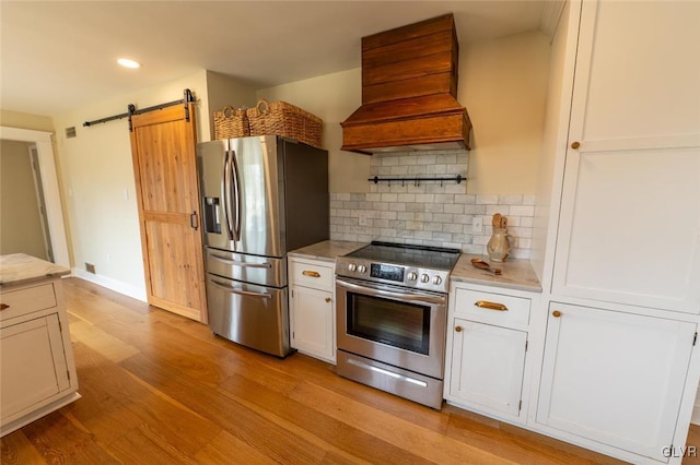 kitchen featuring stainless steel appliances, custom range hood, decorative backsplash, a barn door, and light wood-style floors