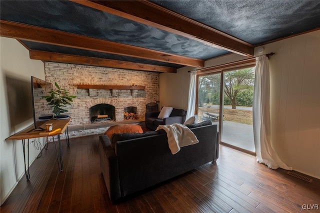 living area featuring a brick fireplace, visible vents, beamed ceiling, and hardwood / wood-style flooring