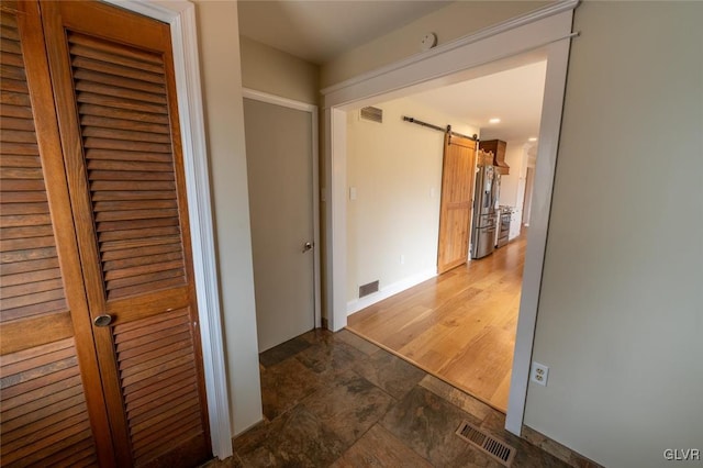 hallway with stone finish floor, visible vents, and a barn door