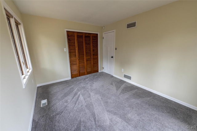 unfurnished bedroom featuring dark colored carpet, a closet, and visible vents