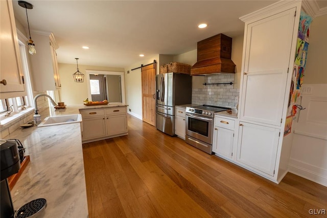 kitchen with stainless steel appliances, custom range hood, a barn door, a sink, and a peninsula