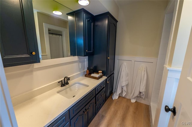 full bath featuring a shower with shower curtain, wainscoting, wood finished floors, vanity, and a decorative wall