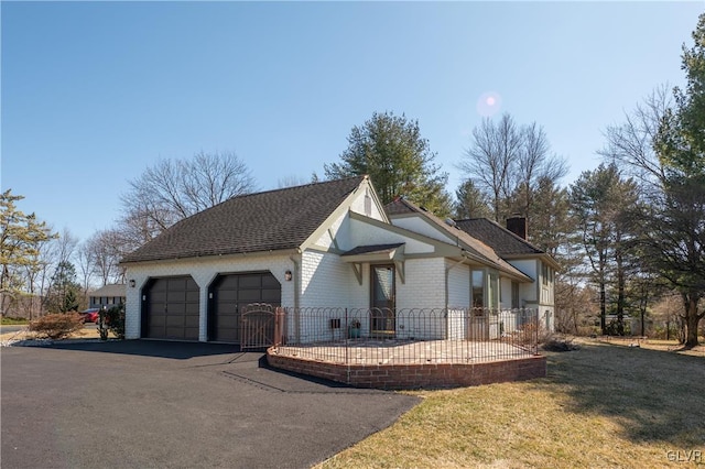 view of front of house with aphalt driveway, an attached garage, brick siding, a chimney, and a front yard