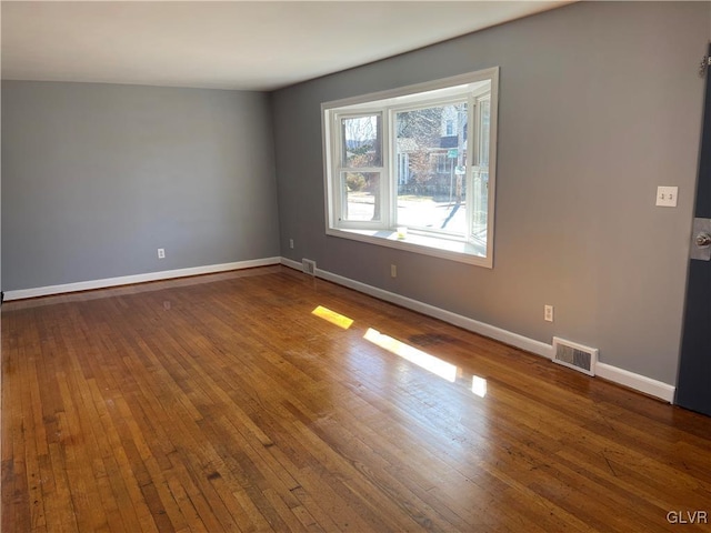 unfurnished room featuring hardwood / wood-style floors, visible vents, and baseboards