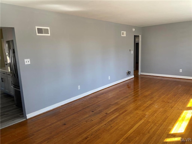 spare room with dark wood-type flooring, visible vents, and baseboards