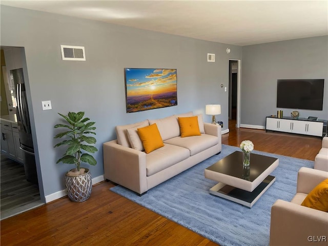 living room with wood finished floors, visible vents, and baseboards